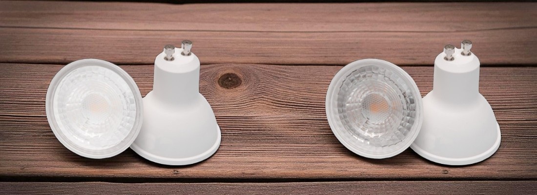 Vier LED-Spotlampen mit GU10-Sockel, jeweils zwei in einem Paar angeordnet, auf einer Holzoberfläche. Jede Lampe ist einmal frontal mit sichtbarem Reflektor und einmal rückseitig mit den Steckkontakten zu sehen.