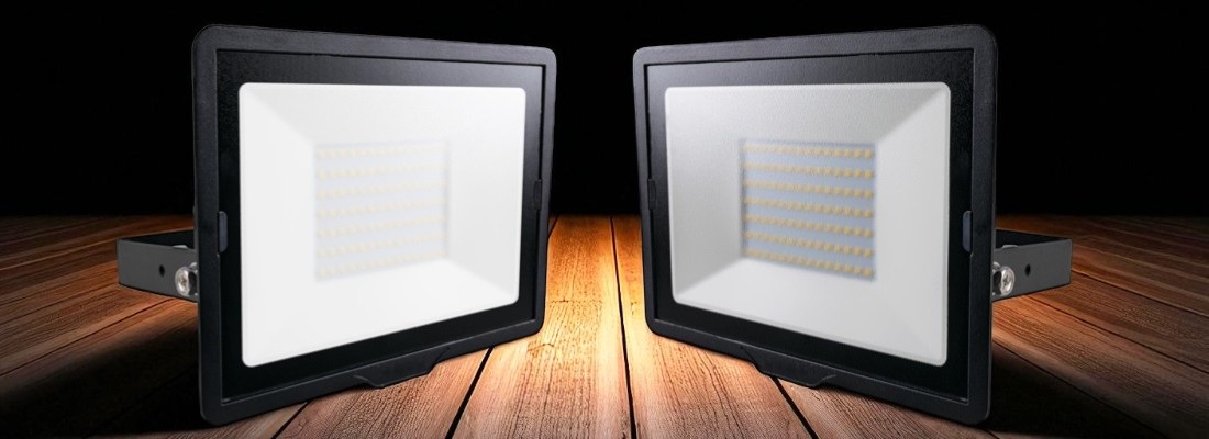 Zwei rechteckige LED-Flutlichtstrahler mit schwarzem Gehäuse, nebeneinander auf einem Holzuntergrund positioniert. Beide Strahler zeigen nach vorne und haben eine grosse Leuchtfläche mit mehreren LED-Reihen. Die Umgebung ist dunkel, wodurch die Strahler im Fokus stehen.