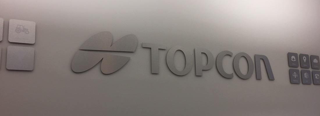 3D Wandlogo aus gebürstetem Aluminium mit Schriftzug Topcon, moderne Firmenwandbeschriftung von Folien Fischer Hamburg, gefertigt für Unternehmen in Bergedorf, Reinbek, Glinde, Wentorf, Lauenburg und Geesthacht.