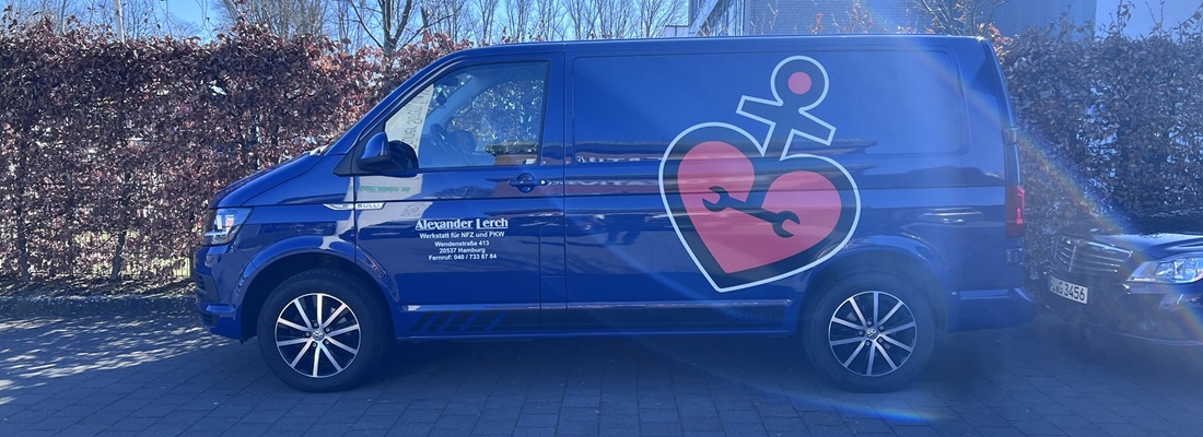 Blauer Handwerker-Transporter mit großem Logo bestehend aus rotem Herz, Schraubenschlüssel und Anker-Symbol. Auf der Fahrertür steht "Alexander Lerch – Werkstatt für KFZ und PKW" mit Adresse und Telefonnummer. Das Fahrzeug steht auf einem gepflasterten Parkplatz bei Tageslicht.
