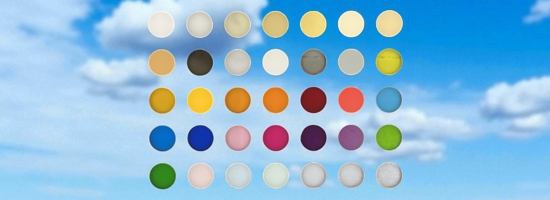 Farbmusterübersicht mit 35 runden Farbfolien, in fünf Reihen zu je sieben Farben angeordnet, vor einem Hintergrund mit blauem Himmel und weissen Wolken. Die Farbtöne reichen von Weiss, Beige und Gelb über Rot, Blau und Grün bis hin zu Grau und Schwarz.