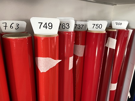 Rote Hochglanz-Folienrollen mit Farbcodes 737, 749, 750 und 763 im Regal – Folien Fischer Hamburg