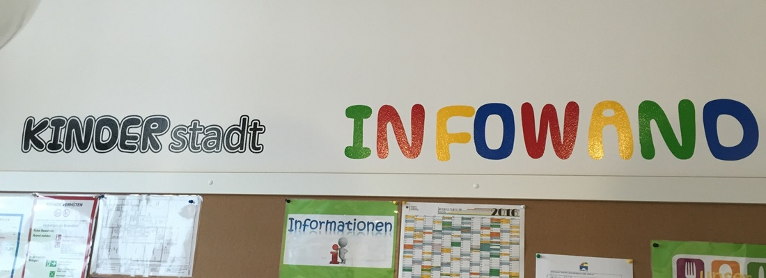 Wandbeschriftung Hamburg: bunte Folienbuchstaben ‚INFOWAND‘ und schwarz-weiße Aufschrift ‚KINDERstadt‘ über Infotafel – Werbetechnik und Folienplot
