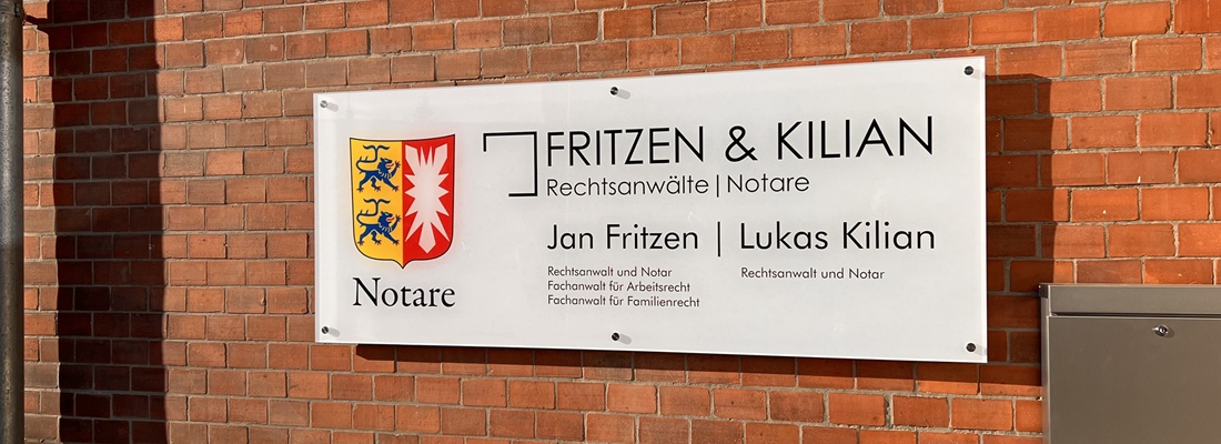 Firmenschild der Kanzlei Fritzen & Kilian, Rechtsanwälte und Notare, an einer roten Backsteinwand. Links das Wappen von Schleswig-Holstein mit der Beschriftung ‚Notare‘. Rechts daneben die Namen Jan Fritzen, Rechtsanwalt und Notar, Fachanwalt für Arbeitsrecht und Familienrecht, sowie Lukas Kilian, Rechtsanwalt und Notar.