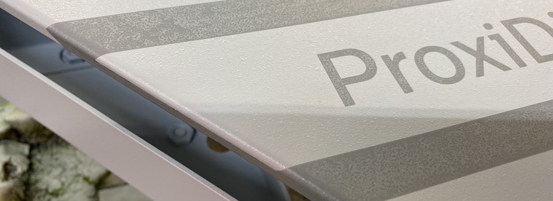 „Nahaufnahme einer weißen Aluminiumplatte mit matter, strukturierter Oberfläche und dem Aufdruck ‚ProxiD‘, teilweise sichtbar.“