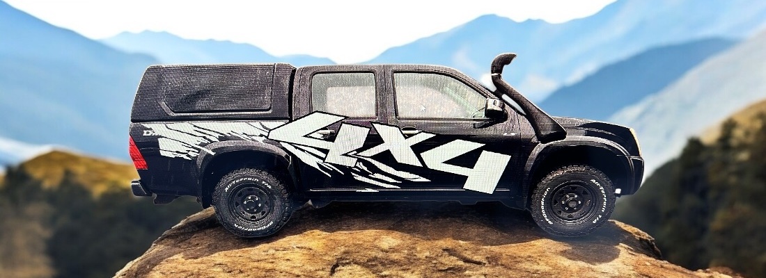 Schwarzer Offroad-Pick-up mit grossem weissem "4x4"-Schriftzug auf der Seite, steht auf einem Felsen mit Berglandschaft im Hintergrund. Das Fahrzeug besitzt Offroad-Reifen, einen Schnorchel und eine Ladeflächenabdeckung.