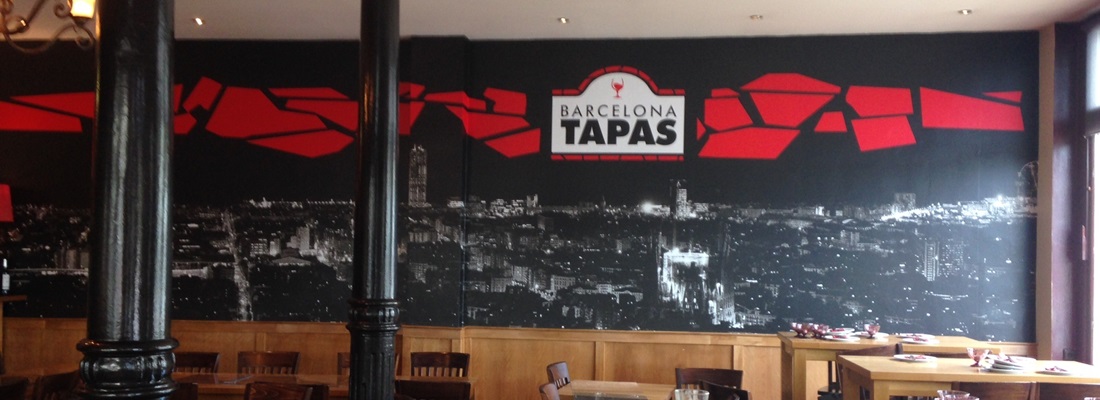 Wandgestaltung mit Folien-Design im Barcelona Tapas Restaurant – schwarze Stadtsilhouette mit roten grafischen Elementen und Logo. Realisiert von Folien Fischer Hamburg Bergedorf für Gastronomie-Innenräume in Reinbek, Glinde, Lauenburg, Geesthacht, reinstorf,Wentorf und Schwarzenbek.